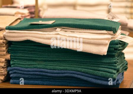 Stack of folded dark teal,blue, and white cotton towels on a wooden shelf in a store or laundry room. Soft textile texture, household linen concept Stock Photo