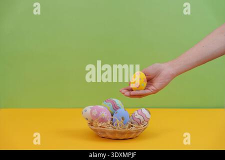 SSTK Easter. Hand holding yellow Easter egg above colorful basket. Stock Photo
