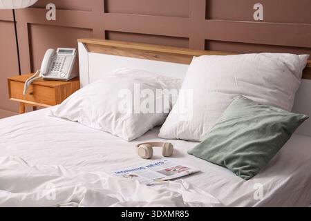 Headphones with newspaper on unmade bed in hotel room Stock Photo