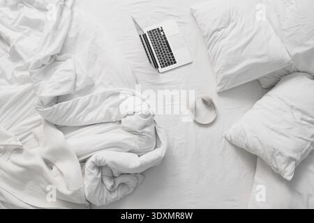 Laptop with headphones on unmade bed in hotel room Stock Photo