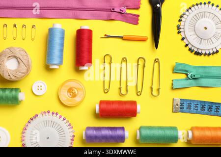 Composition with different thread spools and sewing accessories on yellow background Stock Photo