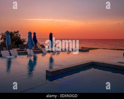 Caribbean sunset with colorful dramatic sky, palm trees reflecting on a beach pool with beach chairs, umbrellas in Curacao Stock Photo