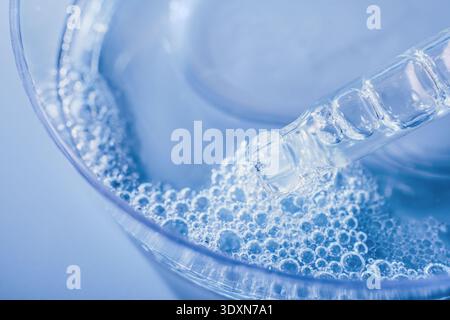 Pipette collecting or dispensing blue liquid into solution creating many small bubbles Stock Photo