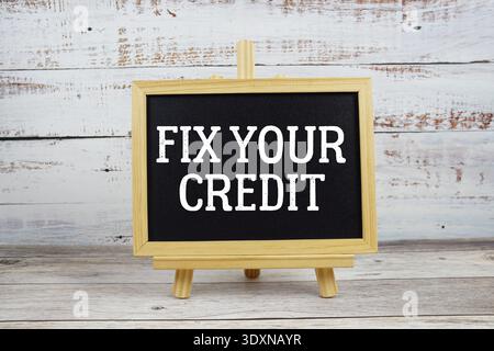 Fix Your Credit text written on blackboard with alarm clock on wooden background Stock Photo
