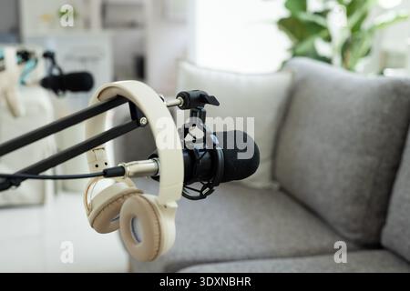Black microphone with foam windscreen is sitting on boom, tan headphones are hanging in home studio Stock Photo