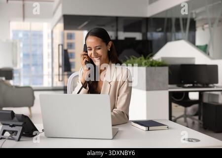 Smiling businesswoman talks on landline phone at workplace Stock Photo