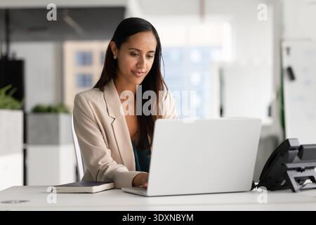 Focused woman working on laptop in contemporary workspace Stock Photo