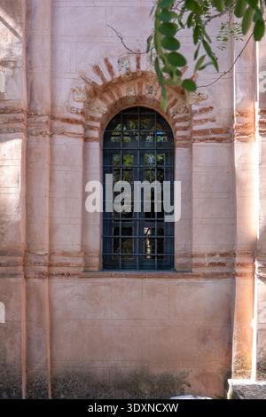 Arched monastery window with iron grating at Nea Moni on Chios island, Greece. Pale stone frame and brickwork in warm earthy colors Stock Photo
