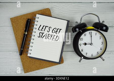 Let's Get Started text written on notepad with alarm clock on wooden background Stock Photo