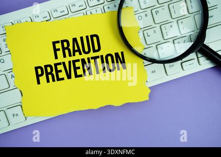Yellow paper with text "Fraud Prevention" and magnifying glass placed on a white keyboard Stock Photo