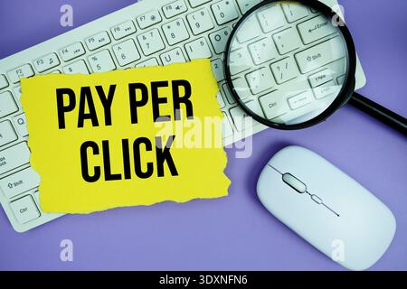 Yellow torn paper with the text "Pay Per Click" placed on a white keyboard, and magnifying glass and a computer mouse Stock Photo