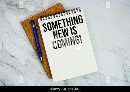Something New Is Coming! text written on notepad with pen on marble background Stock Photo