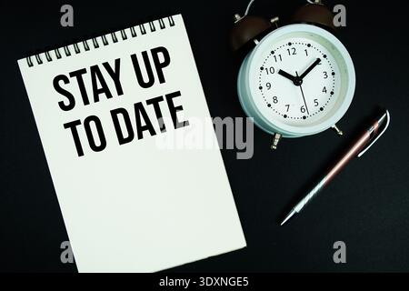 Stay Up To Date text written on notepad with pen and alarm clock Stock Photo
