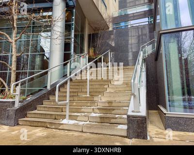 Steps are seen leading to a building entrance with glass and stone features. Snow is present on the stairs. The setting is urban and modern, showing a Stock Photo