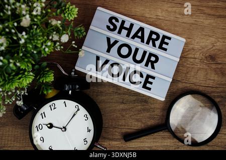 Share Your Voice text in lightbox with magnifying glass and alarm clock flat lay on wooden background Stock Photo