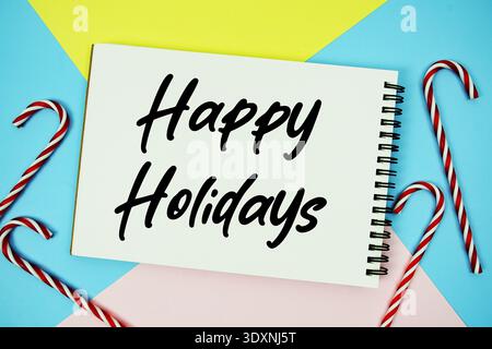 Happy Holidays message of season holidays written on notepad with candy cane decoration on pastel background Stock Photo