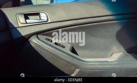 A close view shows the car door panel and window controls. The scene is bright with sunlight shining on the interior while the vehicle is parked. Stock Photo
