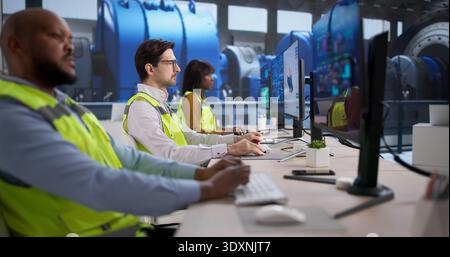An Engineer And Technician Monitor Computer Systems Controlling Energy In Power Plants. A Diverse Team Stock Photo