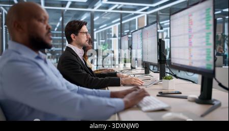 Diverse Team Studies Bills And Data On Computers In Office Setting. People Working With Spreadsheets And Documents Stock Photo