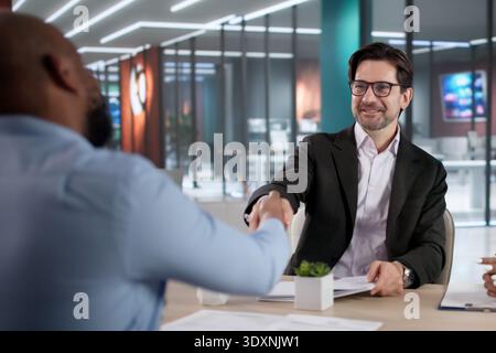 Diverse Team Meets In A Corporate Office, Interviewing And Hiring New Employees. The Recruiter And Manager Shake Hands Stock Photo