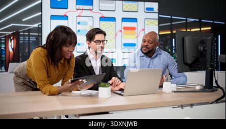 Diverse Team Of Designers And Developers Collaborates On Web Applications Using Laptops And Tablets Stock Photo