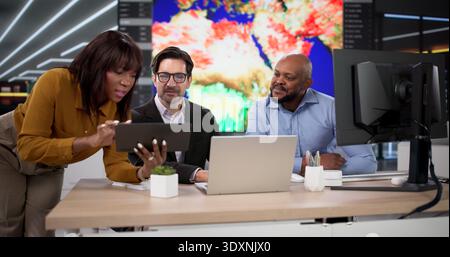 In This Photo, A Diverse Group Of Colleagues Discusses Climate Change Consequences While Using Maps, Laptops Stock Photo