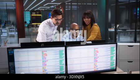 Diverse Team Meets In Office, Analyzing Data On Computers And Spreadsheets. A Professional Coder Works Stock Photo