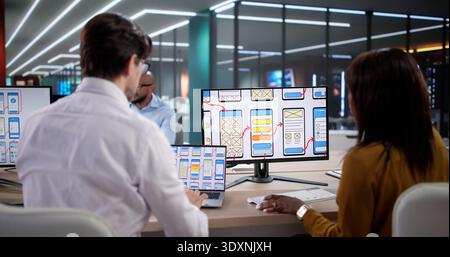 Young Woman Using A Laptop Designs App Interfaces In A Busy Office. An African Man Collaborates With A Diverse Team Stock Photo