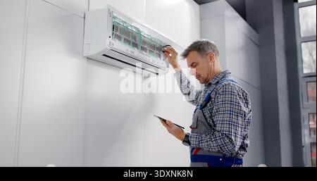 Commercial HVAC Technician Performs Air Conditioner Repair Using Tablet Report. Stock Photo