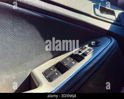 A close-up view shows the control panel of a car door featuring buttons for windows and locks. Sunlight shines on the surface, highlighting the design Stock Photo