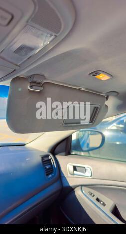 A car is parked with sun visor lowered to block sunlight. The interior shows dashboard and rear view mirror. Daylight is bright, highlighting the feat Stock Photo