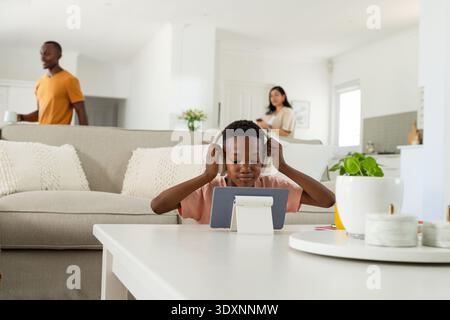 Diverse family gathering in living room with child using tablet on white table, wearing headphones Stock Photo