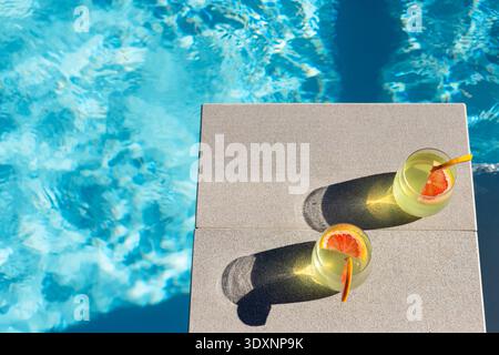 Two stemless glasses sitting on concrete pool coping, casting long shadows and rippling reflections Stock Photo