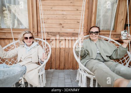 Two Women Relaxing in Hammock Chairs on a Wooden Porch Stock Photo