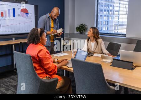 Diverse coworkers in business clothes discussing charts on monitor in conference room with laptops Stock Photo