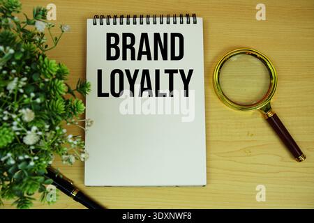 Brand Loyalty text written on notepad with magnifying glass flat lay on wooden background Stock Photo