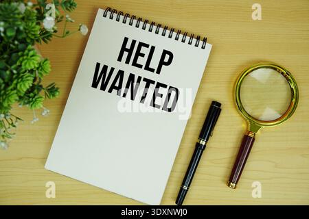 Help Wanted text written on notepad with magnifying glass flat lay on wooden background Stock Photo