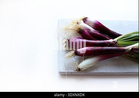Fresh spring onions. A bunch of fresh Tropea red onions on a white cutting board, white background. Healthy, vegetarian food. Stock Photo