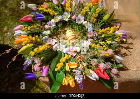 Decorative Easter wreath with colorful spring flowers and a striped egg on a burlap background. Concept of festive holiday home decor, seasonal celebr Stock Photo