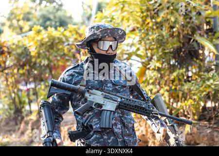 Focused special forces soldier in blue camouflage uniform holding an assault rifle. An operator in tactical gear with boonie hat ready for combat miss Stock Photo