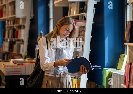 Intelligent woman booklover reading book in cozy bookshop, flipping through pages of publication. Stock Photo