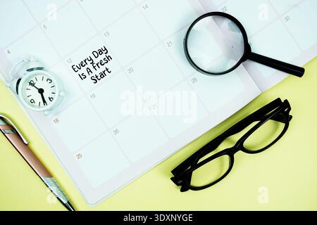 Every Day Is A Fresh Start message written on calendar date with alarm clock, glasses and magnifying glass on yellow background Stock Photo