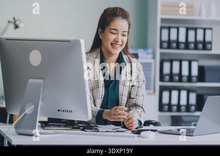 Cheerful business lady working on laptop in office, Asian happy beautiful businesswoman in formal suit work in workplace. Attractive female employee o Stock Photo