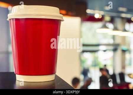 Red disposable coffee cup with lid on table, blurred cafe interior background, takeaway drink branding concept, copy space, shallow depth focus Stock Photo
