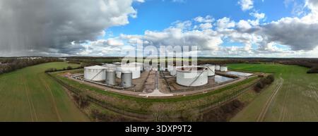 Aerial view of cylindrical white oil tanks contrast against the green fields under a sky of dark storm clouds and patches of blue, Kingsbury, Tamworth Stock Photo