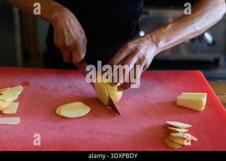 A pastry chef uses a large, sharp knife to cut thin slices of apple for a sweet, cobbler dessert. Stock Photo