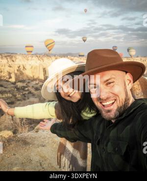Close up Couple of tourists having fun watching hot air balloons from viewpoint smile to camera in Cappadocia at holiday - Happy friends laughing toge Stock Photo