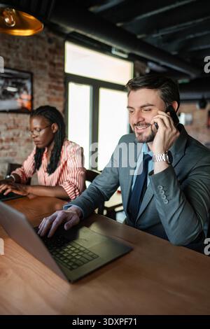 Businessman talking on smartphone while working on laptop Stock Photo