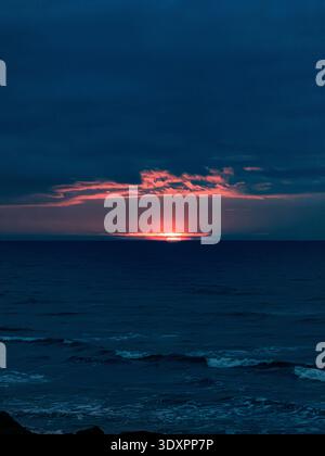 Dramatic winter sunrise over the English Channel from Worthing beach in West Sussex, fiery red sun rising above dark cloud bank across deep blue sea Stock Photo