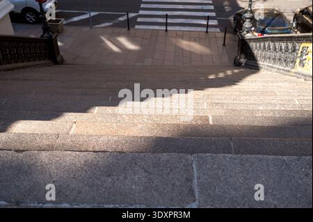 Stone staircase looking down towards a city street with shadows from a decorative railing. Stock Photo